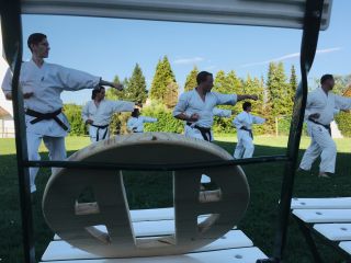Mehrere Karateka trainieren auf einer Wiese. Im Vordergrund ist das Familiensymbol der Familie Mabuni zu sehen.